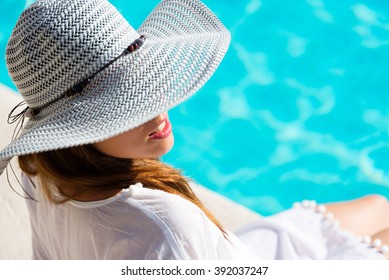 Fashion Pretty Woman On Summer Vacation Relaxing At Luxury Hotel Resort Spa Poolside. Young  Fashionable Lady Wearing Sun Hat And White Kaftan.