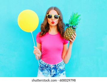 Fashion pretty woman with yellow air balloon and pineapple wearing a pink t-shirt over colorful blue background