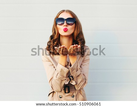 Fashion pretty young woman blowing red lips sends sweet kiss wearing a black sunglasses coat over grey background
