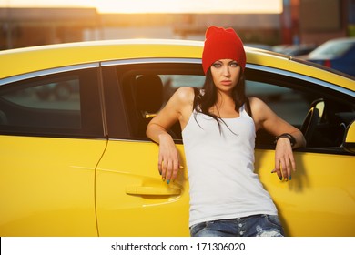 Fashion punk woman leaning on her car Stylish female hipster model in white tank top and red beanie