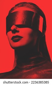 Fashion and sci-fi concept. Abstract woman studio portrait with make-up and big futuristic metallic glasses or helmet covering her eyes. Model wearing dark blouse. Toned image with red and black color