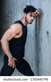 Fashion Shoot Of A Handsome And Sexy Indian Or Arab Looking Male Fitness Model With A Gym Fit Body And Black Curly Hair And A Stylish Small Beard Posing Against A Grey Concrete Wall