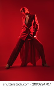 Fashion Shoot. Portrait Of A High Fashion Female Model Posing With Expression In Red Suit, Red Chiffon Cloth Wrapped Around Her Head And Black Sunglasses. Studio Shot On A Red Background.