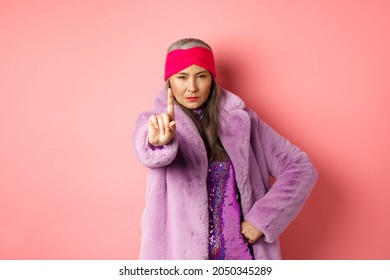 Fashion And Shopping Concept. Serious Asian Senior Woman Showing Not So Fast Gesture, Shaking Extended Finger To Stop Or Warn You, Looking Determined At Camera, Wearing Stylish Purple Clothes