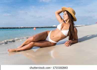 Fashion shot of a beautiful girl in a white bikini lying on the beach.