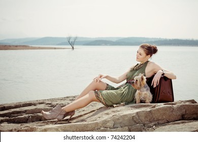 Fashion Shot Of A Beautiful, Professional Model On The Lake With A Suitcase And A Dog (Yorkshire Terrier)