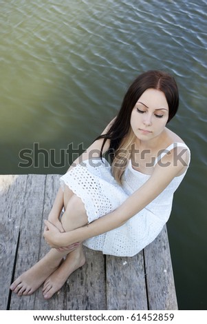 Fashion shot of beautiful woman wearing white sitting alone on the pier