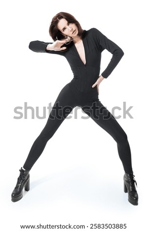Fashion shot. Full-length portrait of a slender fashion model girl posing in black tight-fitting overall and black boots. White studio background.