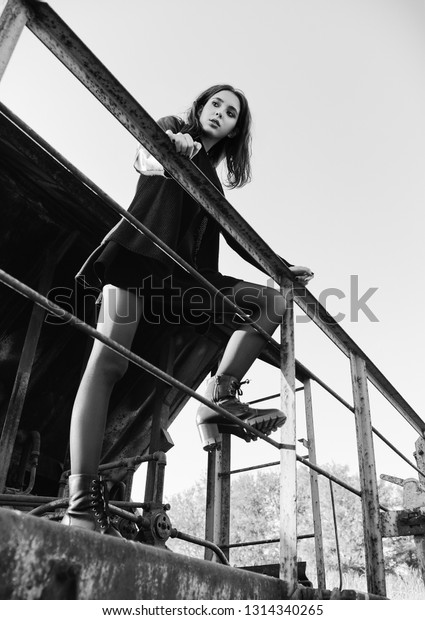 Fashion shot: portrait of the lovely rock girl\
(informal model) dressed in black jacket and skirt standing on\
train car. Black and\
white