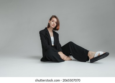 Fashion Shot Of Stylish Vogue Woman In Black Suit Sitting On Floor In Studio