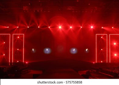 Fashion Show Catwalk Runway Stage in Reddish atmosphere with smoke, spotlight par lighting in red color over hanging construction with black walk way and vdo camera dolly with empty seat, copy space - Powered by Shutterstock