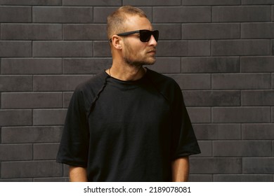 Fashion street portrait of handsome man hipster with cool stylish sunglasses in trendy t-shirt poses near a black modern brick background - Powered by Shutterstock