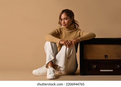 Fashion Studio Photo Of Elegant Woman Wearing Warm Sweater Sitting Near Vintage Radio Isolated On Beige Background