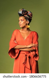 Fashion Studio Photo Of Stylish African Woman With Turban And Orange Dress Posing  Over Green Background. 