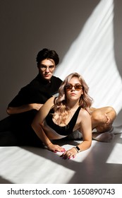 Retrato de estudio de moda (hermosa pareja de modelos hombres y mujeres con anteojos tirados en el suelo) al estilo de campaña de Calvin Klein