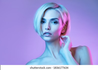 Fashion studio portrait of a woman with short blond hair  in colourful neon lighting on purple background.  