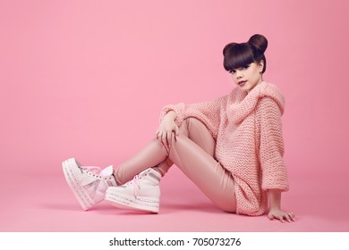 Fashion studio teen look style in shoes. Fashionable young girl wears in wool sweater and leather pants sitting on the floor isolated on pink background.