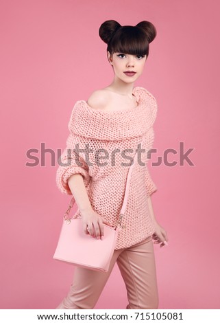Fashion studio teen look style with casual handbag. Fashionable young girl wears wool sweater and leather pants posing isolated on pink background.