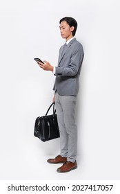 Fashion And Style. Full Body Young Man In Gray, Suit ,tie And White Shirt ,pants, Brown Shoes Use A Mobile Phone Holding Handbag In Studio

