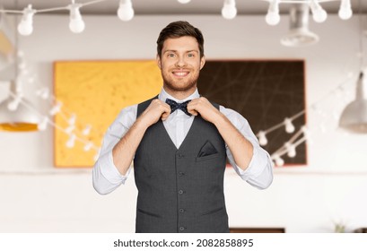 fashion, style and holidays concept - happy man in festive suit dressing for party and adjusting bowtie over restaurant background