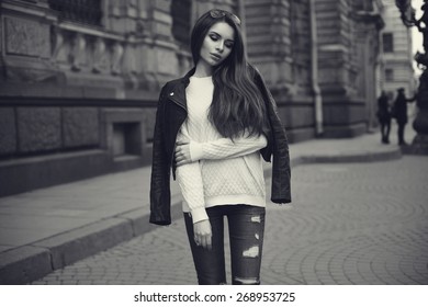 Fashion style portrait of young beautiful calm female model posing at city street with magnificent architecture. Monochrome portrait.