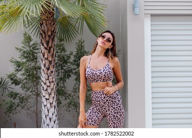 Fashion Stylish Fit Tanned European Woman In Sunglasses, Leopard Cami Top And Biker Shorts, Outside Villa Near Palm Tree. 