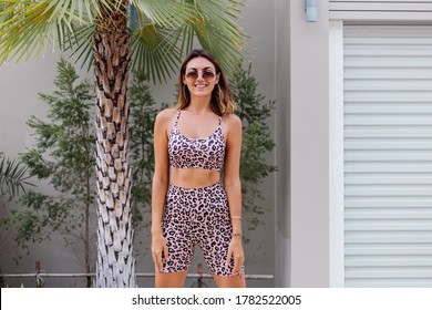 Fashion Stylish Fit Tanned European Woman In Sunglasses, Leopard Cami Top And Biker Shorts, Outside Villa Near Palm Tree. 