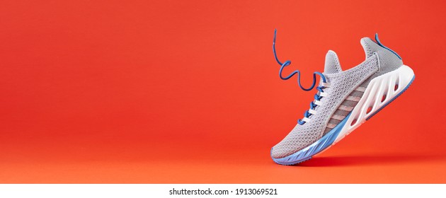 Fashion stylish sneakers with flying laces. Running sports shoes on orange background. Close up.