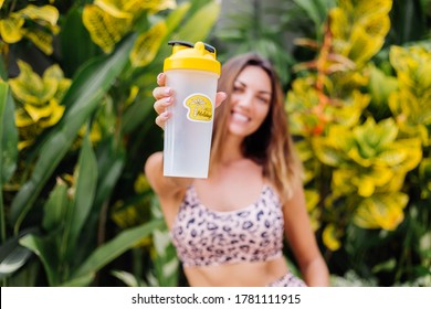 Fashion Stylish Young Caucasian Fit Sporty Woman In Leopard Cami Top And Biker Shorts Outside Holds Protein Shaker, Bottle Of Water, In Hand. Female With Abs After Jogging Thirsty For Water.