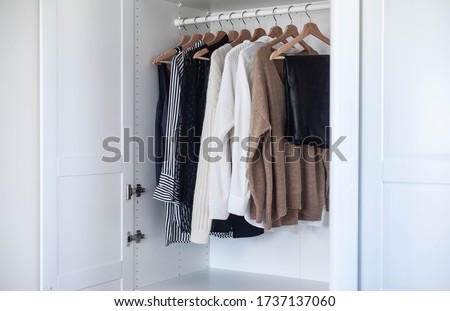 Fashion stylist clothes basic wardrobe.Neutral colors: white, black, beige. White closet, wooden hanger shoulders.