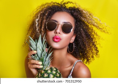 Fashion summer portrait afro american girl in sunglasses and pineapple over yellow background