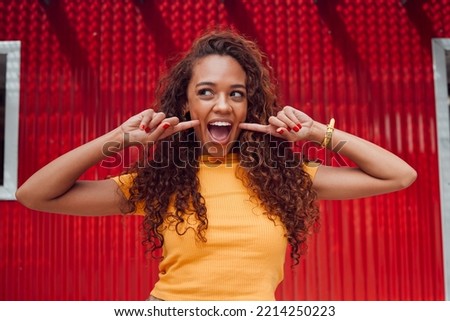 Fashion, summer and woman with smile on red background in city. Beauty, freedom and happy girl on holiday touching face in cute, silly and goofy pose. Excited, happiness and adventure in urban town