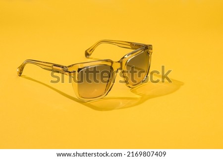 Fashion sunglasses in sunlight on summer pastel yellow background. Woman stylish eyeglasses for banner. Transparent plastic glasses. Sunglass in creative concept