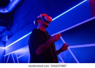 Fashion tech man with VR headset glasses with joysticks playing game in dark room with neon light