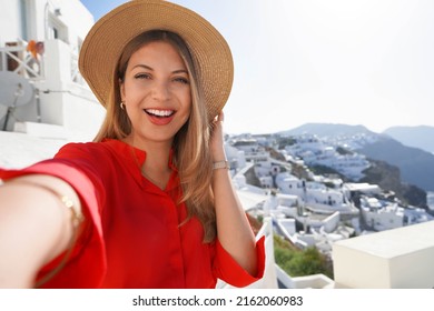 Fashion traveler girl taking selfie photo in Oia picturesque greek village of Santorini Island. Young woman enjoying holidays in Greece, Europe.