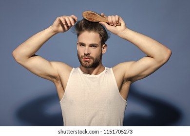 Fashion, Underwear, Style. Man Brush Hair With Hairbrush On Blue Background. Haircare, Hairstyle Concept. Beauty, Grooming, Hygiene. Macho With Bearded Face And Haircut In White Singlet.