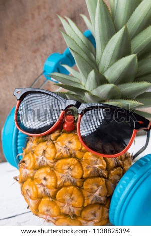 Fashion whole pineapple with sunglasses and headphone listens to music on sack and white wooden background