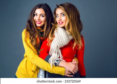 Fashion winter portrait of blonde and brunette beautiful best friends girls, hugs and having fun. Wearing bright stylish cashmere sweaters and scarfs. Have trendy make up and long amazing hairs.