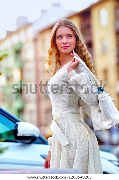 Fashion woman in autumn spring dress with\
flared skirt on city street. Female style feminine fashionable girl\
model with outdoor. Color tone car and building on shiny sunlight\
background.