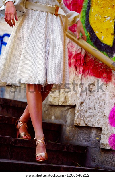 Fashion woman in autumn spring dress on city\
street. Cropped shot of female feet. Low section girl model\
wallking hight heel fall steps outdoor. Color tone on shiny\
sunlight graffiti wall\
background.
