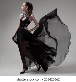 Fashion Woman In Fluttering Black Dress. Gray Background.