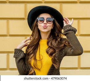 Fashion Woman In A Hat And Sunglasses, In Knit Dress And Jacket Outdoors In The Fall.Blowing Lips Kiss.