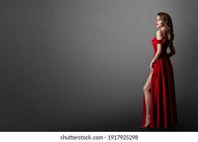 Fashion Woman in Long Red Dress. Model Showing Leg in Evening Silk Slit Gown. Side Profile View. Black Background with Copy Space