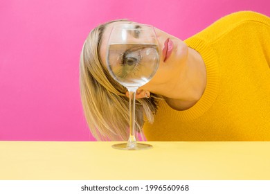 Fashion woman portrait, eye looks through the glass of water. Object distortion, optical illusion. Minimalistic contemporary art.Beautiful woman's face in wine glass.Visual concept.