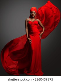 Fashion Woman in Red Dress and Hijab. African Model in Evening long Gown with flowing Silk Fabric over Dark Gray background. Muslim Bride in Wedding chiffon Veil