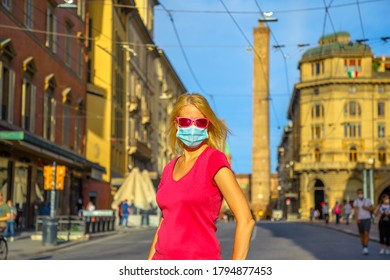 Fashion woman with a surgical mask and sunglasses with Two Towers building at sunset in Bologna town. COVID-19 Coronavirus after quarantine lockdown of Bologna city in Italy.
