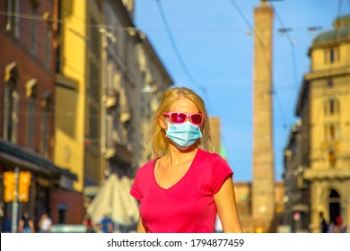Fashion woman with a surgical mask and sunglasses with Two Towers building at sunset in Bologna town. COVID-19 Coronavirus after quarantine lockdown of Bologna city in Italy.