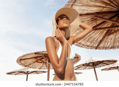 Fashion woman wear sun straw hat under beach umbrella of straw concept of summer beach holiday, vacation travel or sun skin care protection, banner with copy space for text or logos on sky background - Powered by Shutterstock