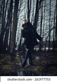 Fashion woman wearing a winter coat and she standing in a gloomy forest, cold rainy weather, cross processed full length image