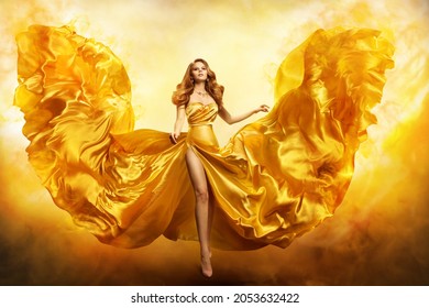 Fashion Woman in Yellow Gown. Fantasy Girl in Golden Dress Flying on Wind like Phoenix Wings in Fire over Fiery Art Background